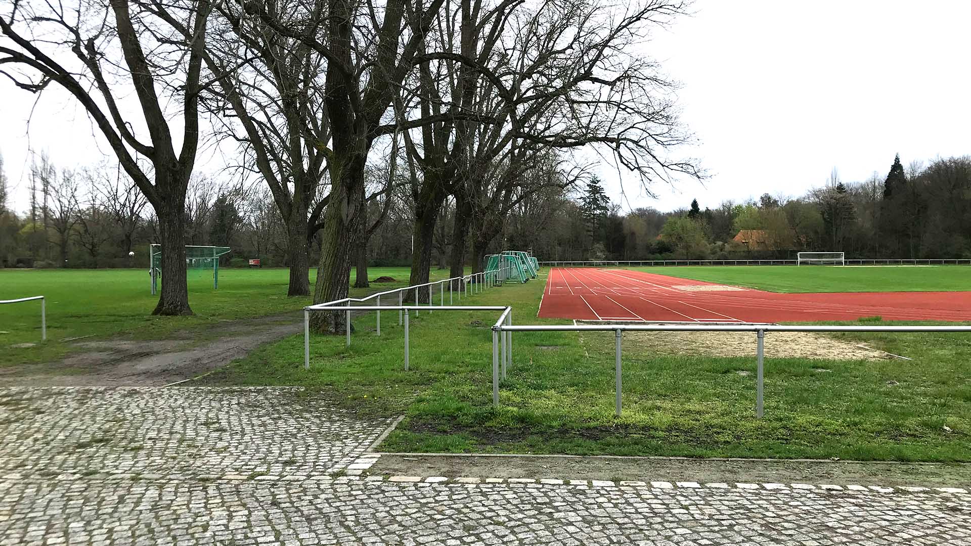 Blick auf die Kampfbahn auf der rechten Bildhälfte. Auf der linken Bildhälfte sind zwei Baumreihen zu sehen , die die räumliche Abgrenzung zu den mittleren Sportplätzen bilden.